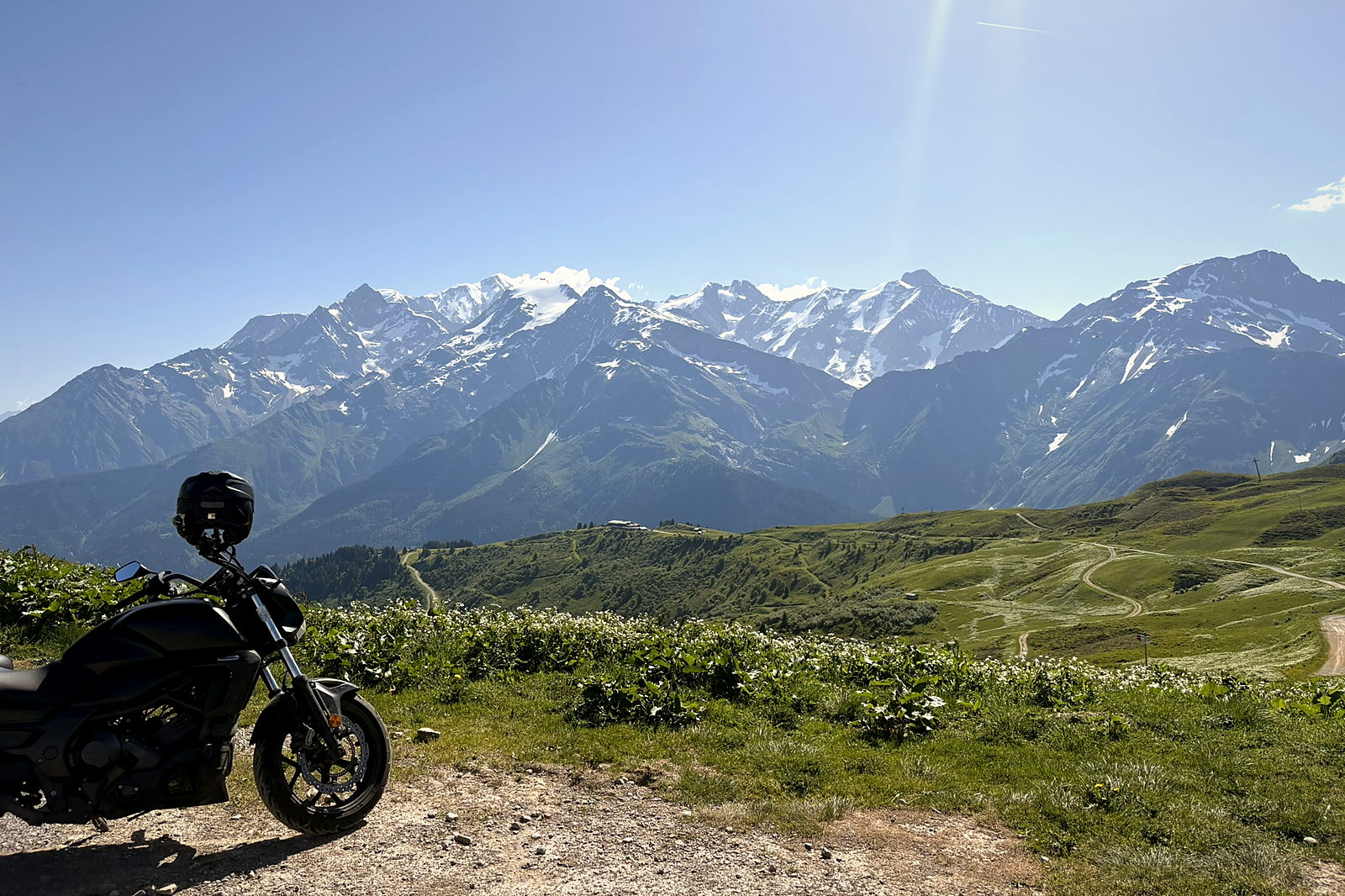 A motorcycle parked at the Col du Joly with a snow-capped alpine range on the horizon